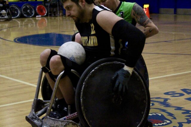 Men playing wheelchair rugby on an indoor court.