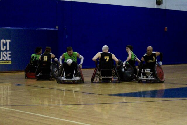 Men playing wheelchair rugby on an indoor court.