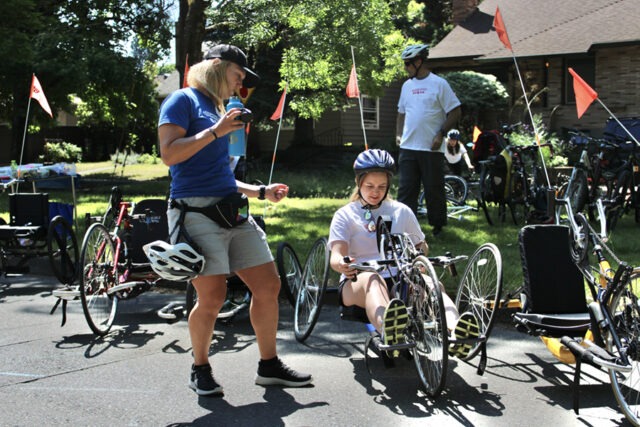 Woman trying out a hand cycle near a volunteer.