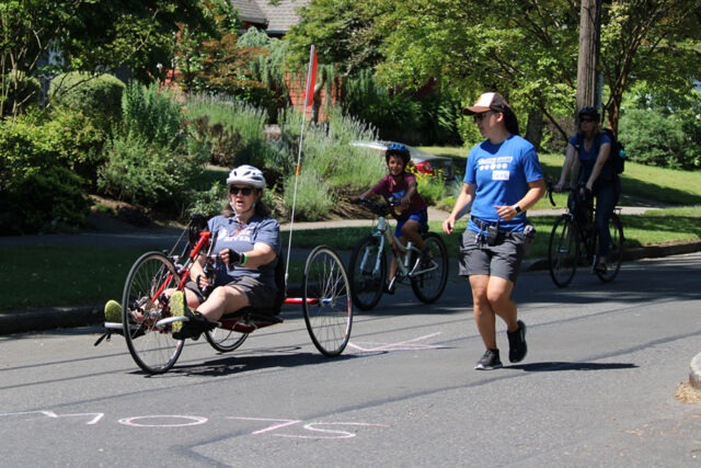 Woman riding a handcycle in a road race next to a volunteer.