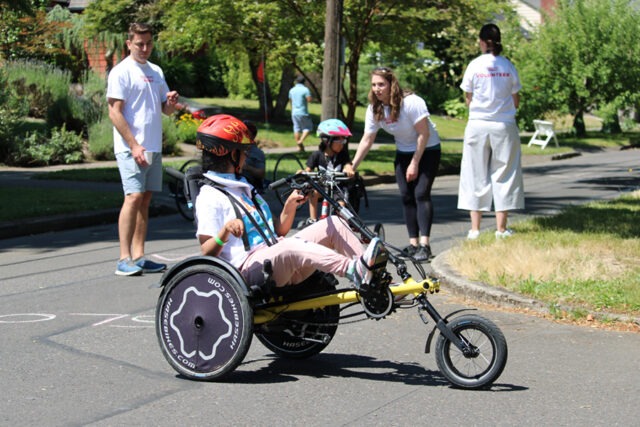 Woman on an adaptive cycle in a road race with volunteers.