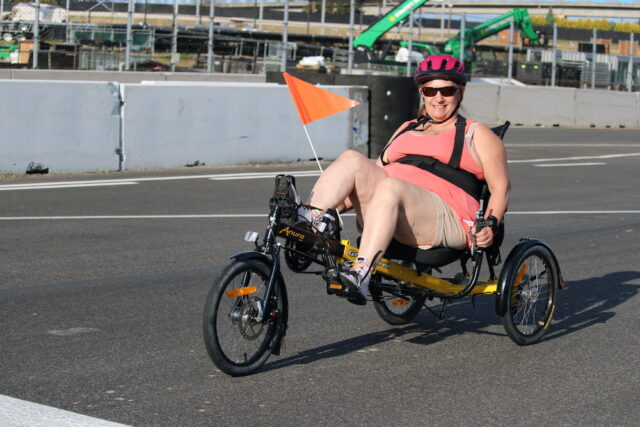 Woman riding a handcycle on an outdoor track.