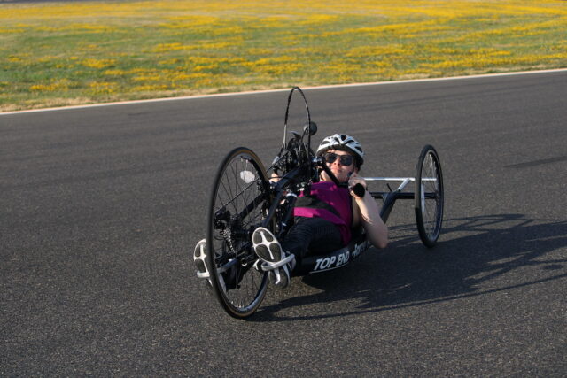 Woman riding a recumbant handcycle on an outdoor track.