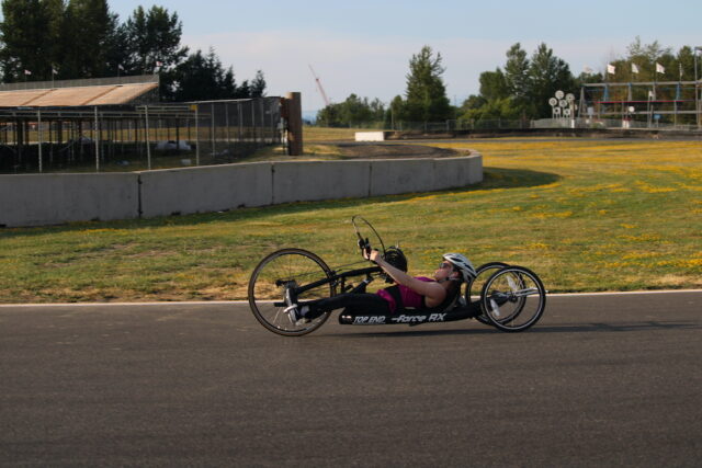 Woman riding a recumbant handcycle on an outdoor track.