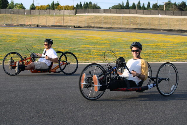 People riding handcycles on an outdoor track.