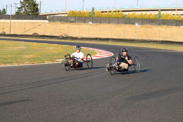 People riding handcycles on an outdoor track.