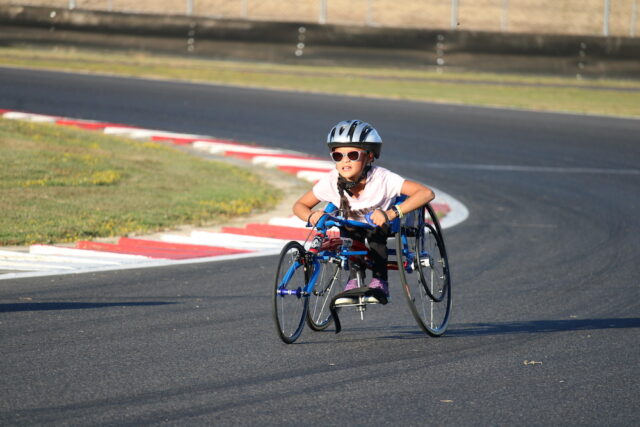 Child riding a handcycle on an outdoor track.