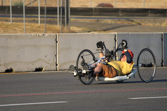 Man riding a recumbant handcycle on an outdoor track.
