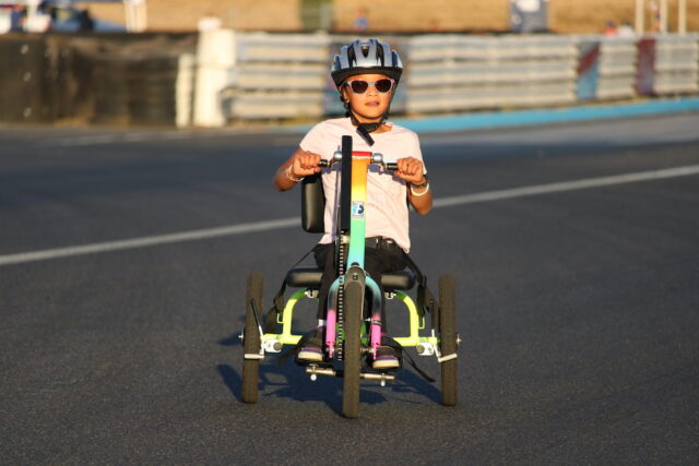 Young girl riding a handcycle on an outdoor track.