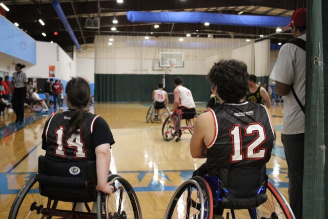 Two wheelchair basketball players watching a game from the sideline.