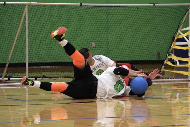 Goalball players blocking the ball on the floor.