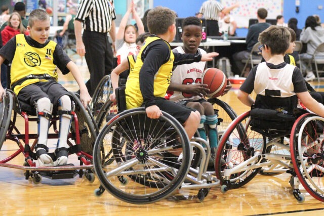Youth wheelchair basketball game on an indoor court.