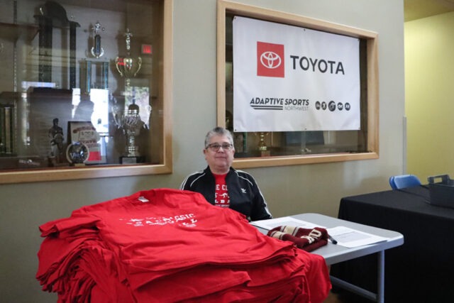 Person sitting near pile of red t-shirts.