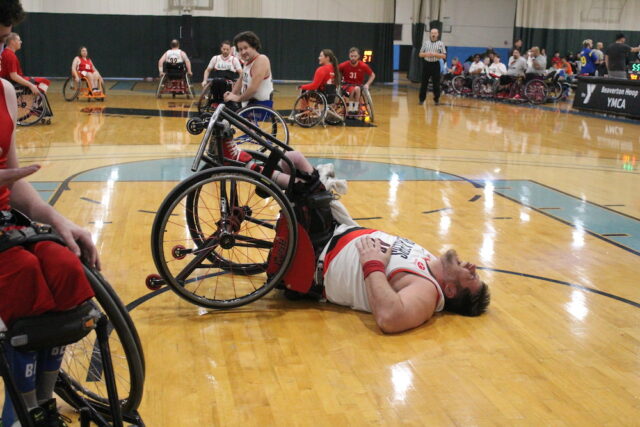 Young wheelchair basketball player fallen and laughing on an indoor court.