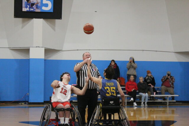 Youth wheelchair basketball game on an indoor court.