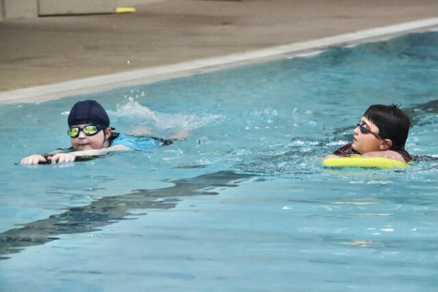 Two young swimmers with kickboards in a pool.