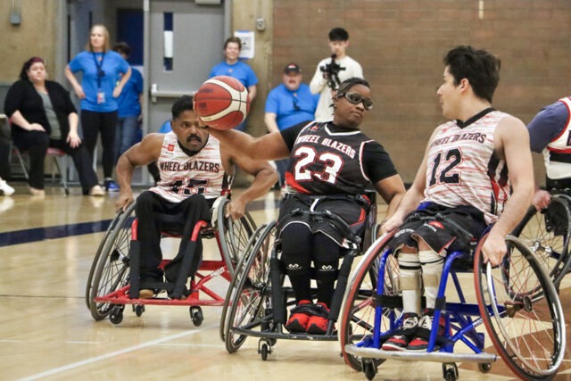 Men and women Blazers playing wheelchair basketball indoors.