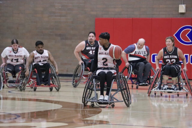 Men and women Blazers playing wheelchair basketball indoors.