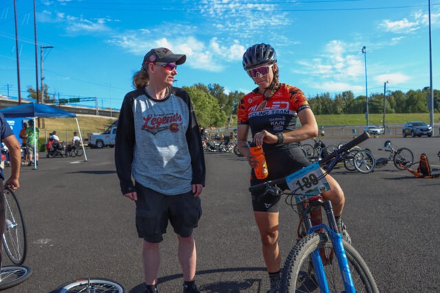 Two women at an outdoor ASNW event, one sitting on a bicycle.