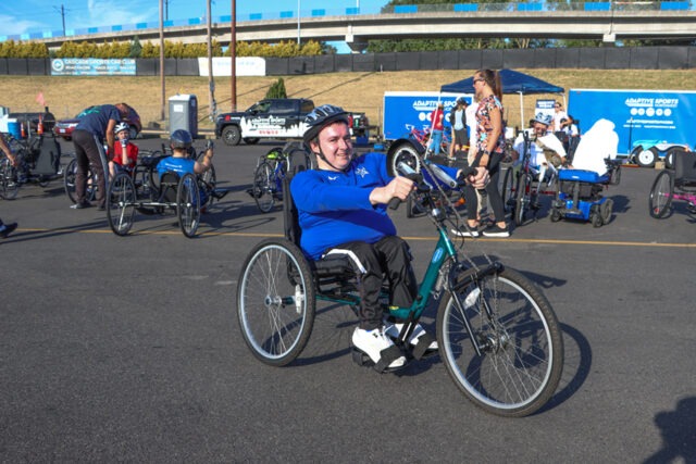 Smiling man sitting in a hand cycle at an ASNW outdoor event.