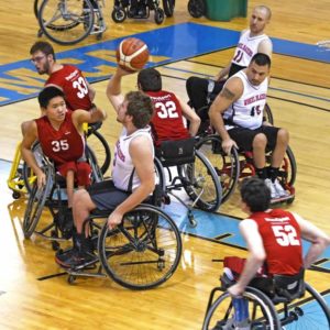 Adult wheelchair basketball game on an indoor court.