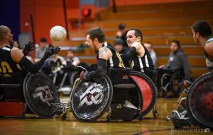 Men playing wheelchair rugby on an indoor court.