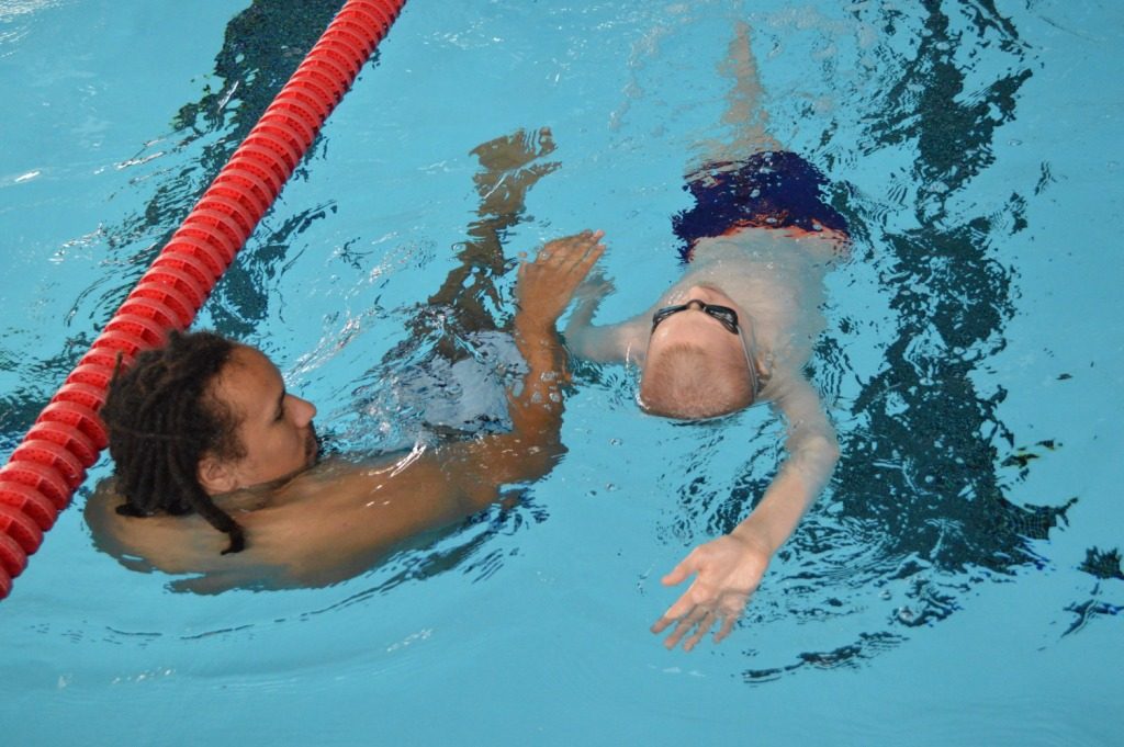 Swimming student practicing backstroke with coach.