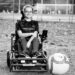 Grayscale photo of young woman in power wheelchair with power soccer guard and ball.